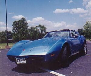 front-side view of the 1976 Corvette, with a fresh blue paint job, parked in a parking lot on a sunny day